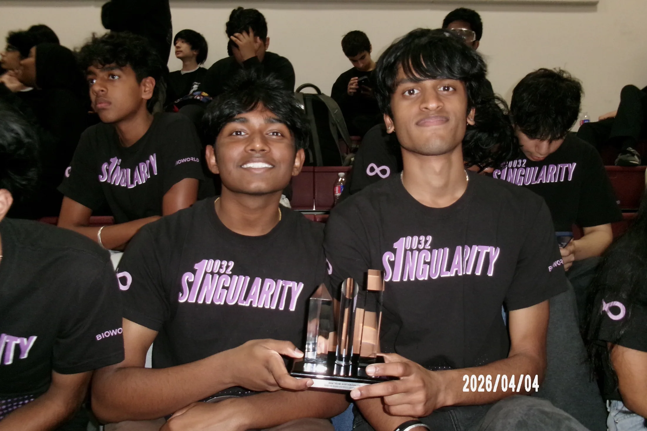 Two students holding a trophy, crowd behind
